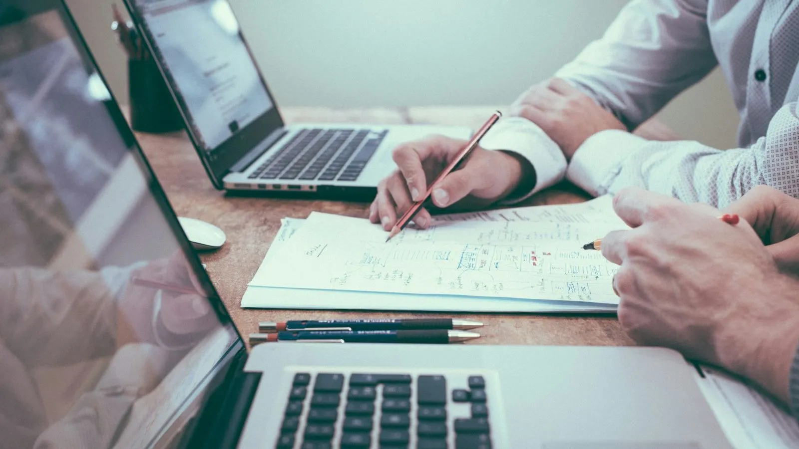 Duas pessoas analisando documentos e planilhas entre notebooks