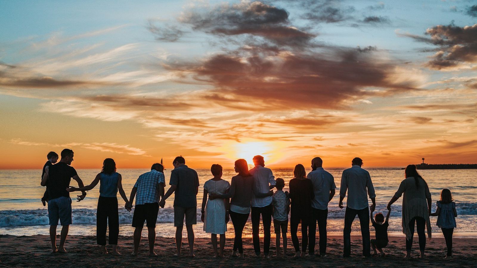 Família reunida de mãos dadas observando o pôr do sol na praia