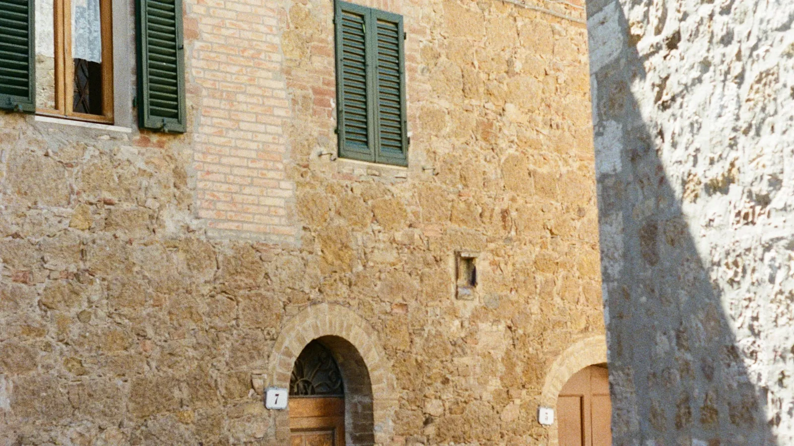 Fachada de casa antiga de pedra com venezianas verdes e porta em arco