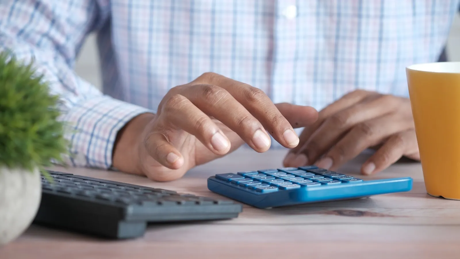 Mãos de uma pessoa usando calculadora sobre mesa de trabalho